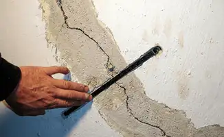 A wall with a large crack is being inspected by a professional in Lowell, MA